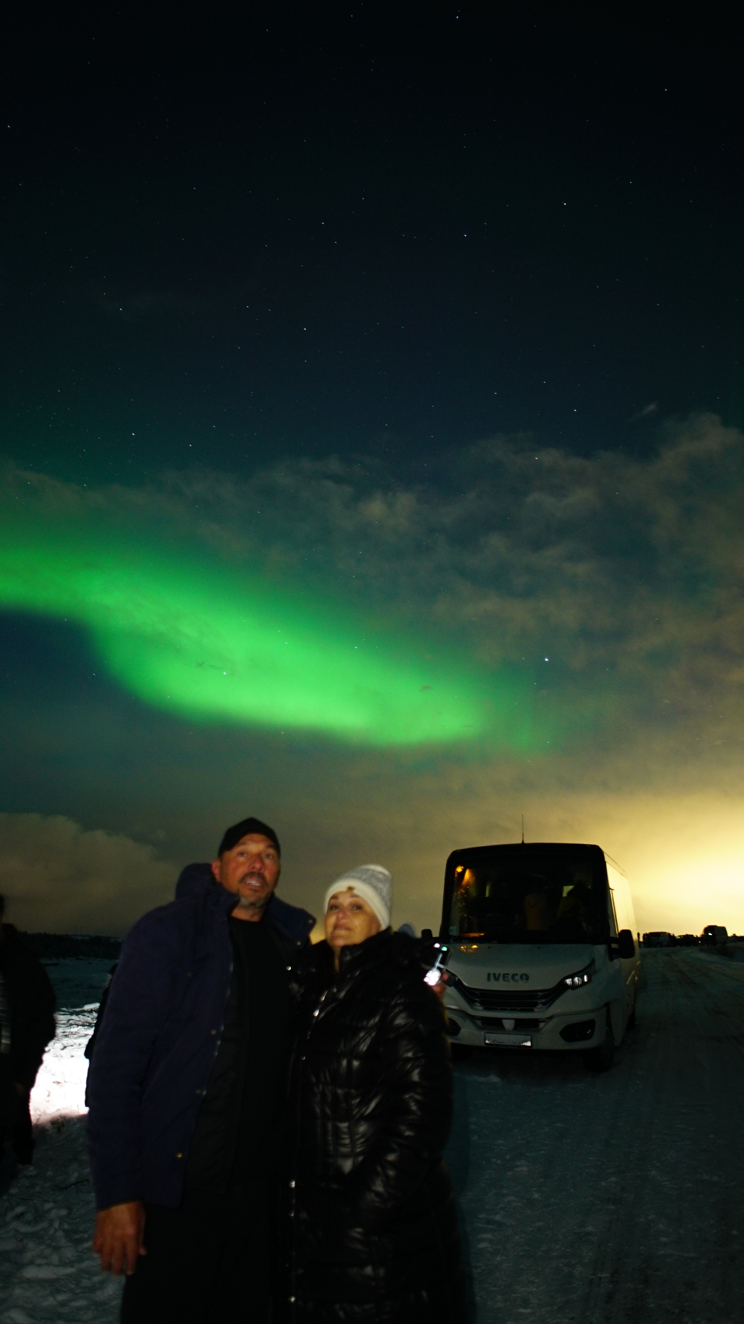 Pareja bajo la aurora junto al vehículo de expedición