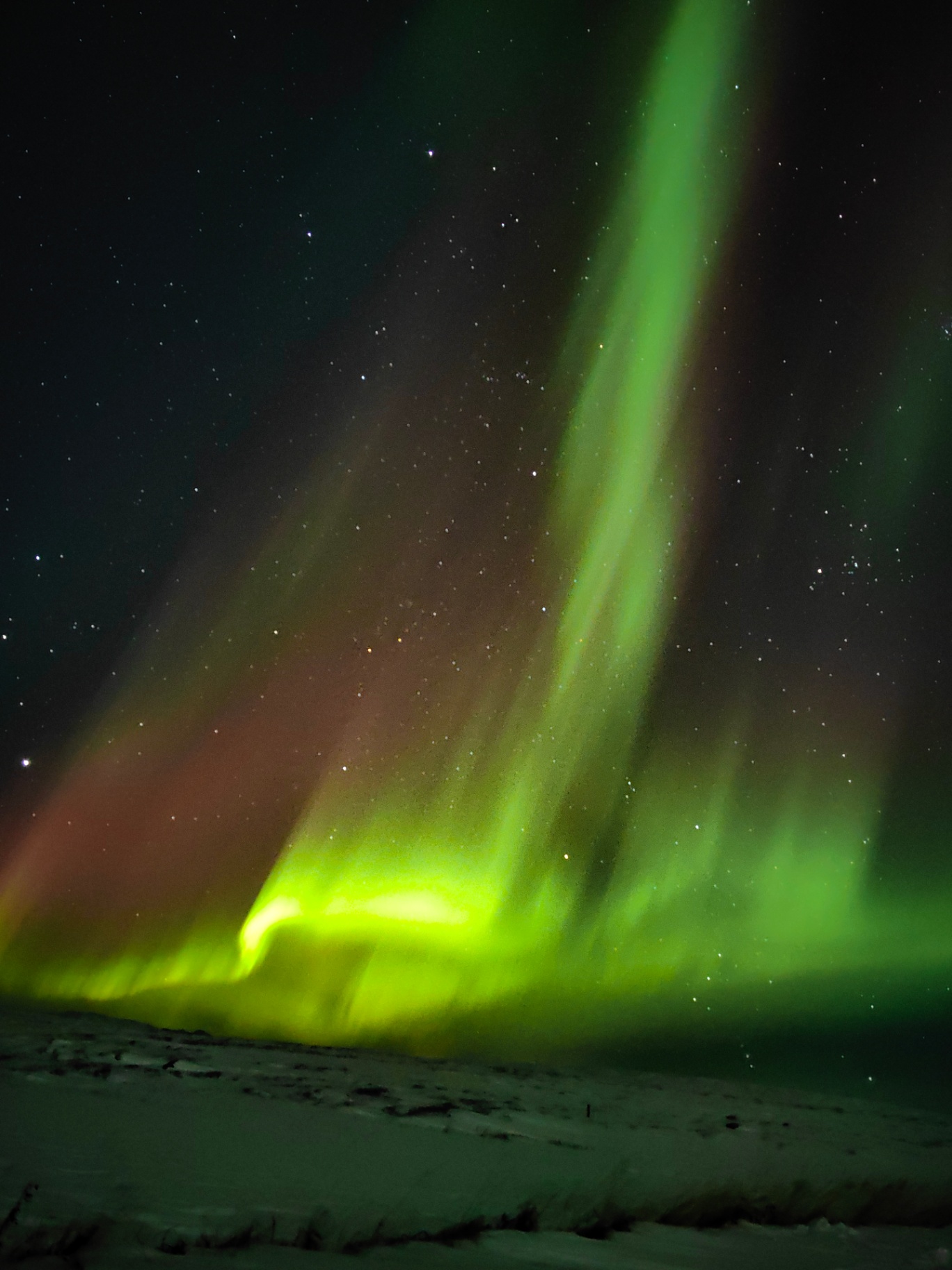 Rayos verticales de aurora verde y rojiza sobre nieve