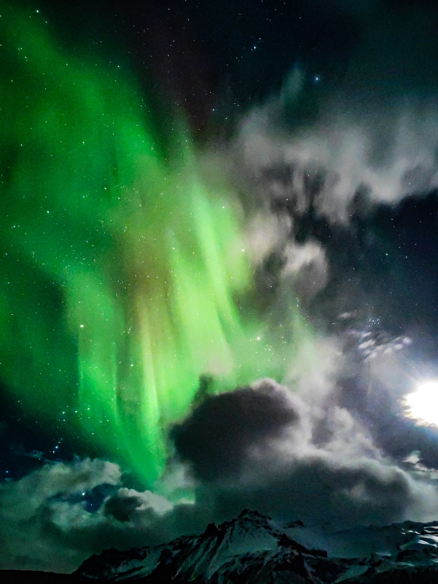 Aurora sobre pico nevado entre nubes