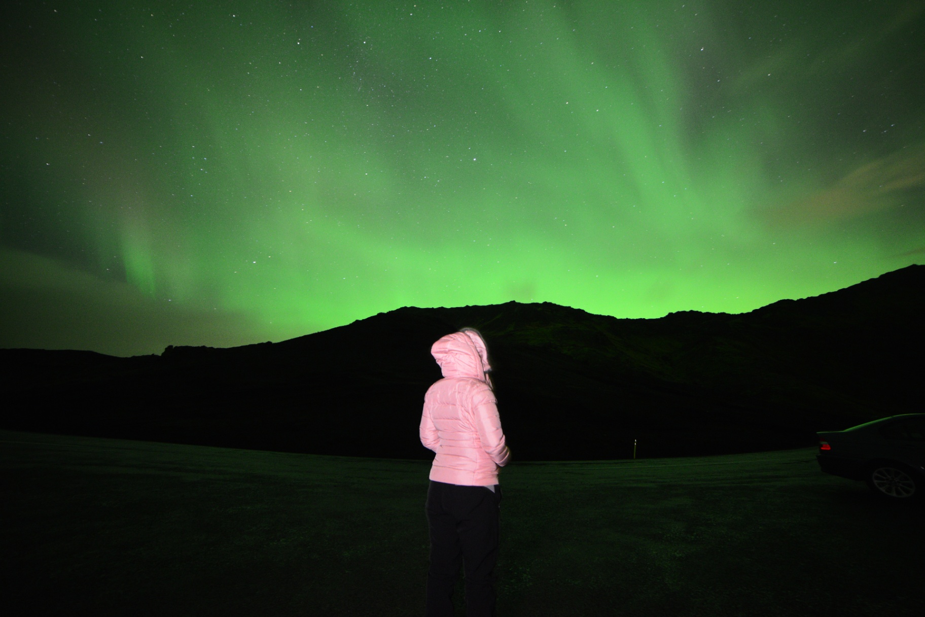 Viajera bajo aurora verde sobre montañas
