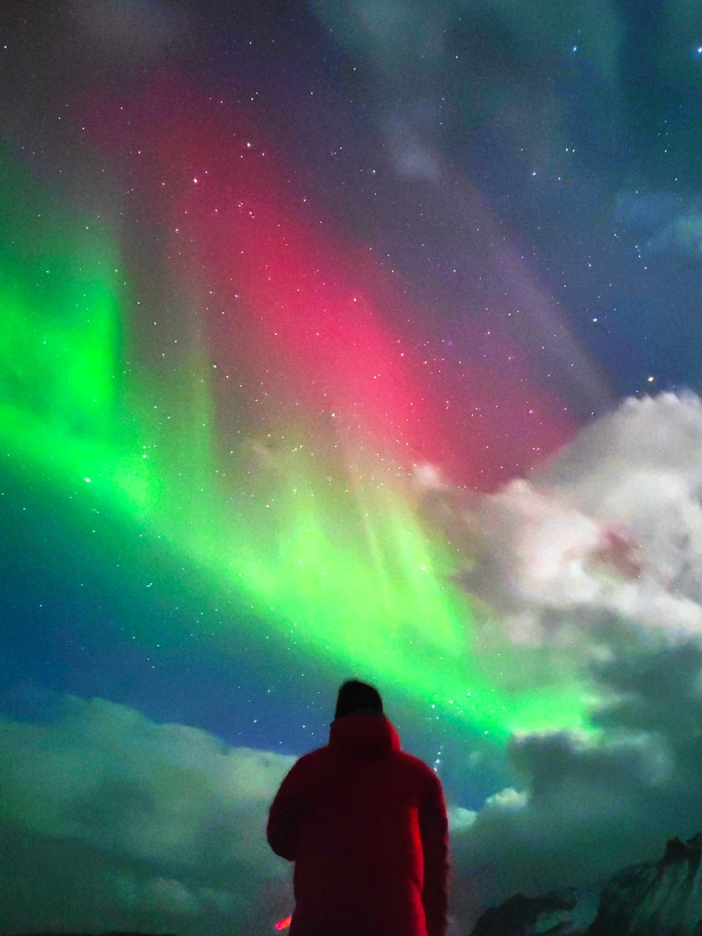 Aurora roja y verde sobre viajero con parka roja